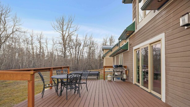 A wooden deck with a table and chairs, a grill, and a sliding glass door leading to a covered area. - Tight Lines (Red Lodge)