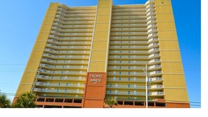 Un hotel de gran altura con múltiples balcones y un cartel llamativo que dice "TROPIC WINDS".