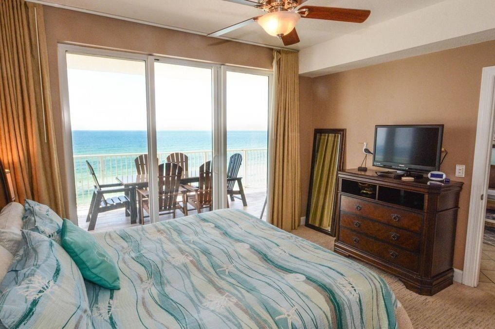 A bedroom with a bed, a television, a dresser, and a balcony with chairs.