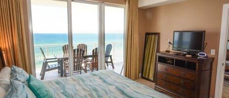 A bedroom with a bed, a television, a dresser, and a balcony with chairs.