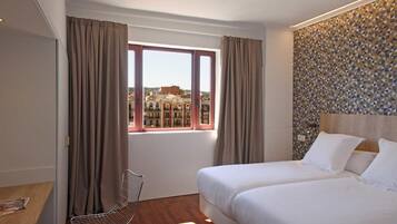 A hotel room with two beds, a window with curtains, a chair, and a patterned wall.