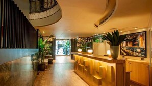 A modern hotel lobby with a wooden reception desk, potted plants, and a staircase.