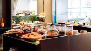 A buffet with various food items, including pastries and bread, displayed on a counter with a view of a cityscape through large windows.