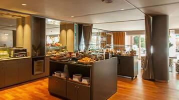 A modern hotel room with a wooden floor, a large window, and a kitchenette area.