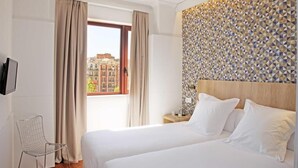 A hotel room with a large bed, a view of buildings through a window, and a geometric wall design. - Chic and Basic Velvet (Barcelona)