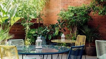 An outdoor patio with a brick wall, green plants, and a round table with chairs.