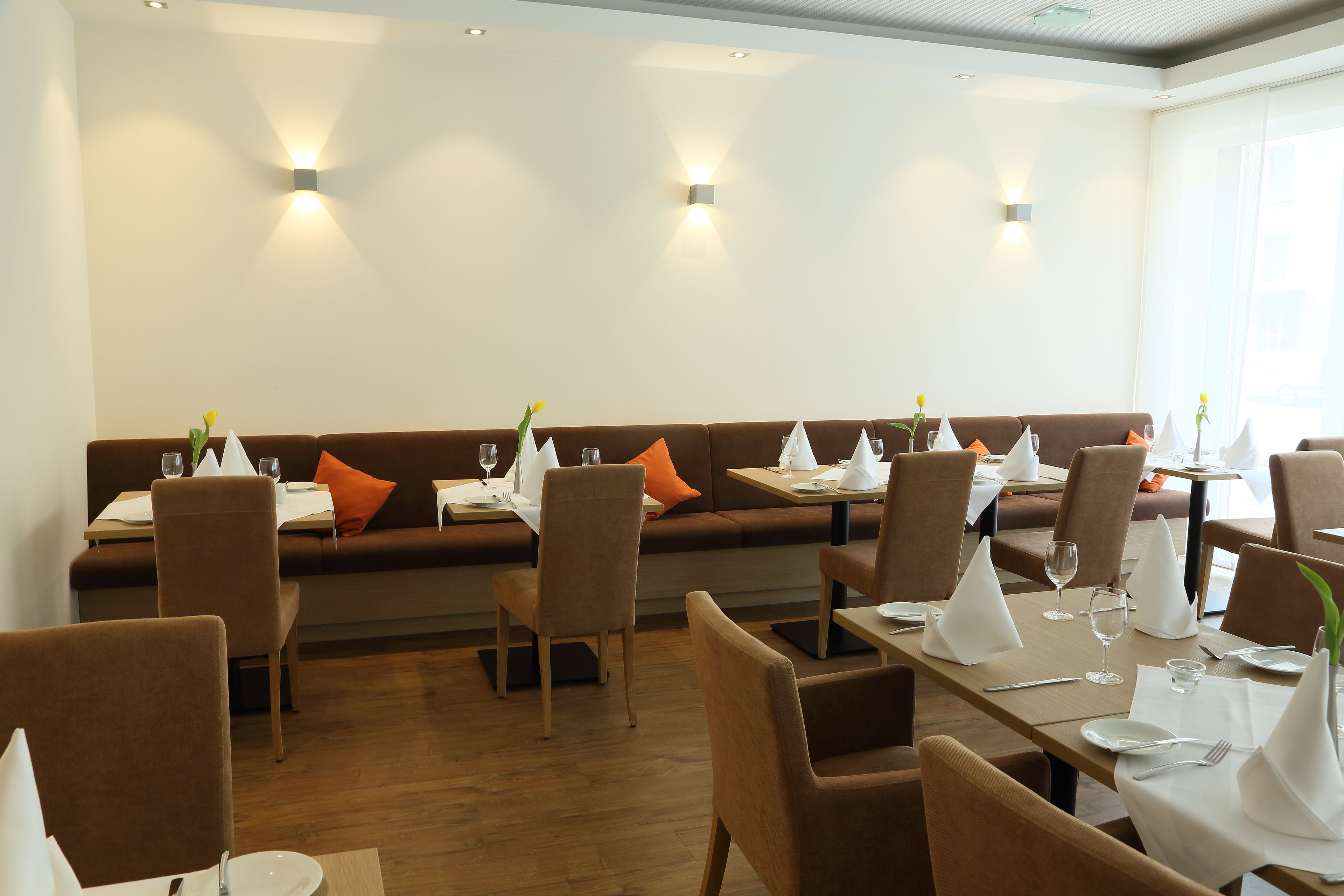 Ein Restaurant mit einem langen Tisch, braunen Stühlen und einer Couch mit orangefarbenen Kissen.