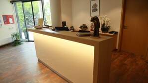 A reception desk with a laptop, phone, and decorative items. There is a door and a plant in the background. - Ardey Hotel (Witten)