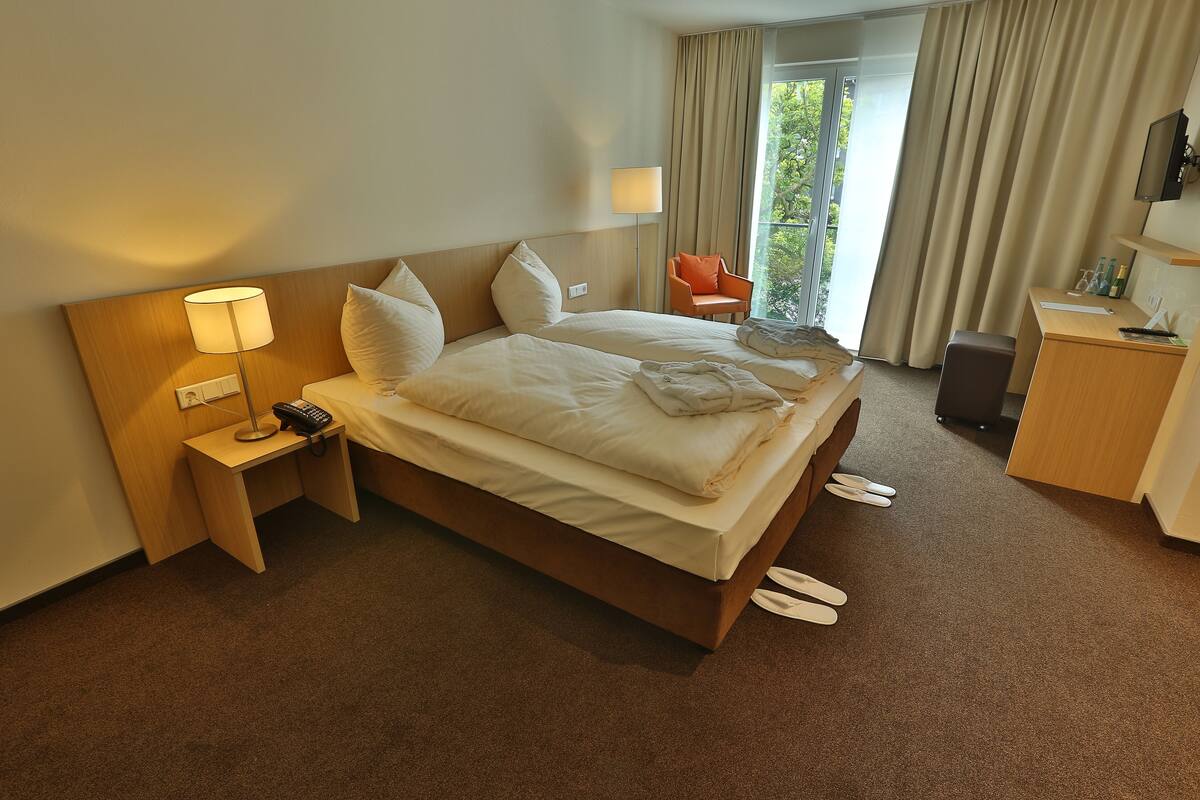 A hotel room with a large bed, a desk, a chair, a lamp, and a view of the outdoors.