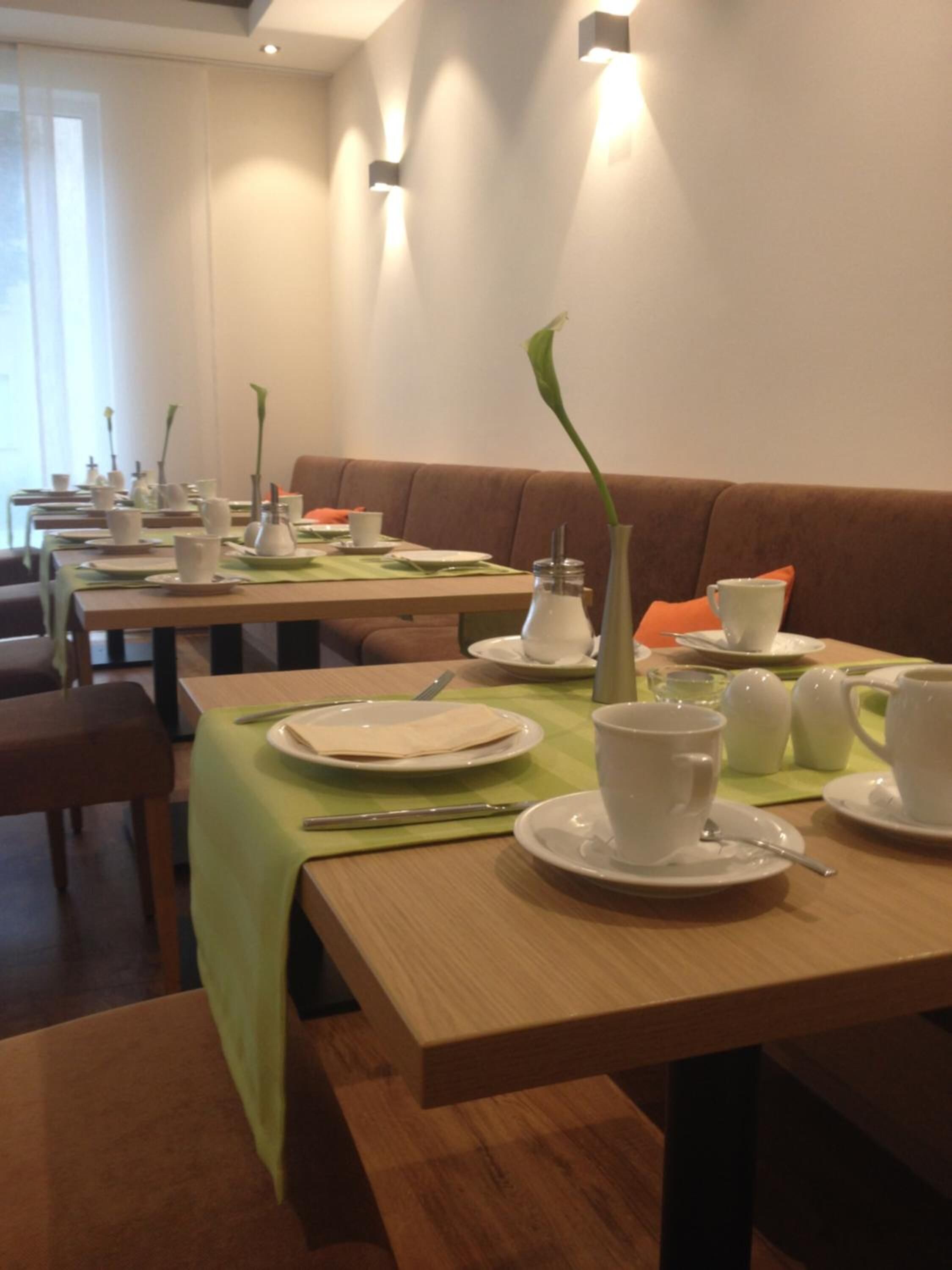 Un espace repas avec plusieurs tables préparées pour le petit-déjeuner, chacune étant mise avec des assiettes, des tasses et des couverts.