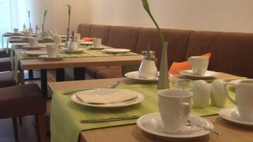 Un espace repas avec plusieurs tables préparées pour le petit-déjeuner, chacune étant mise avec des assiettes, des tasses et des couverts.