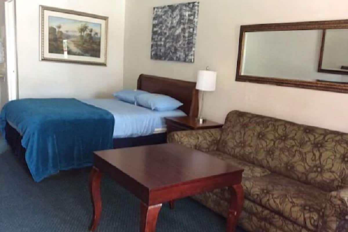Una habitación con una cama, un sofá, una mesa, una lámpara y un cuadro en la pared.