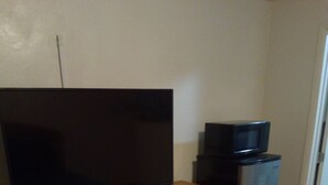 Un dormitorio con un aparador de madera, televisor, refrigerador y una cama con manta azul.