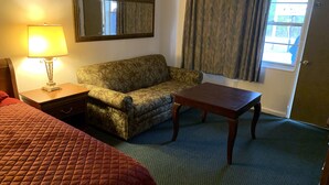 Una habitación de hotel con cama, sofá, mesa, lámpara, espejo y ventana con cortinas.