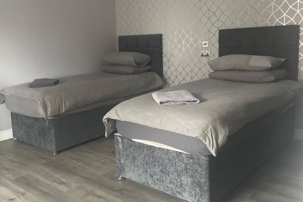 A bedroom with two beds, a patterned wall, and wooden flooring.
