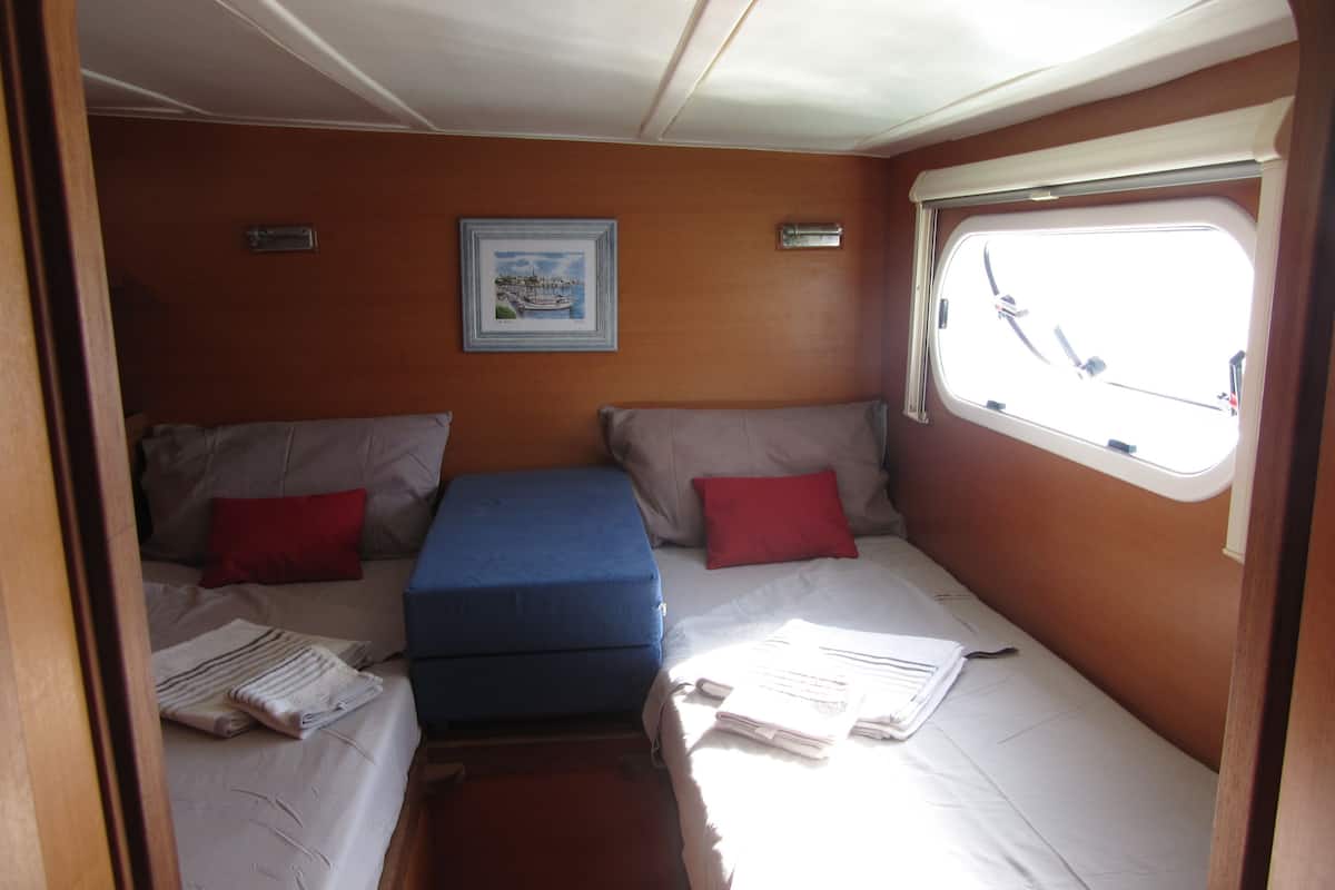 A compact cabin with two beds, each with pillows and folded towels. There is a small table in the center and a window on the right.