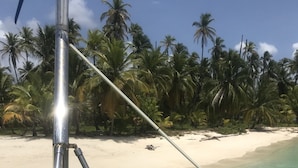 A beach scene with clear turquoise water, a person swimming, and palm trees in the background. - iCan Sailing Experience (Turneffe Islands)