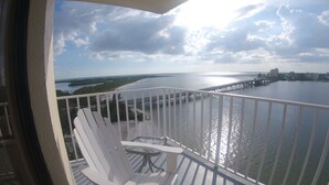 A balcony with white railings, a glass table, and two white Adirondack chairs overlooking a body of water with a pier extending into it. - Lovers Key Beach Club by Lovers Key Vacations (Fort Myers Beach)