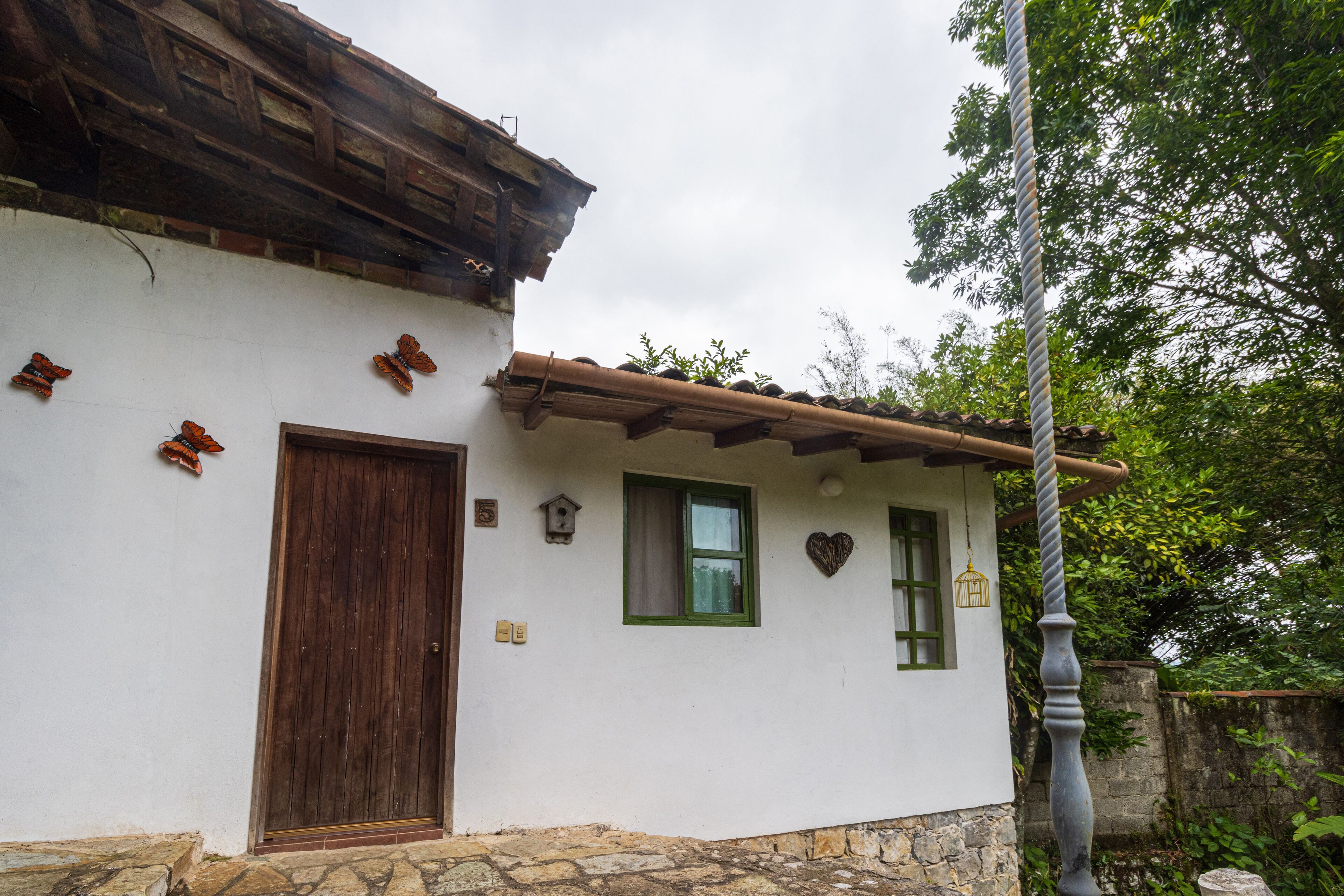 A rustic building with a wooden door, a window with a green frame, and a heart-shaped decoration on the wall.