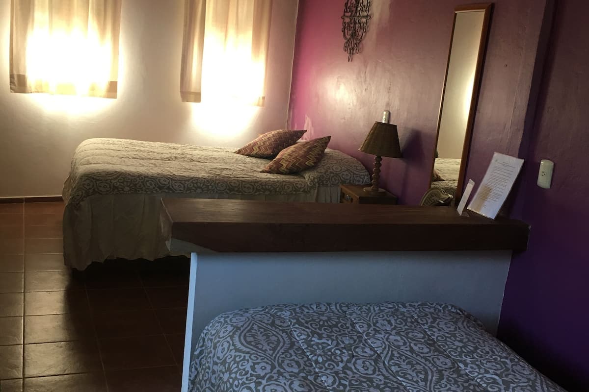 A room with two beds, a ceiling fan, and a purple accent wall.
