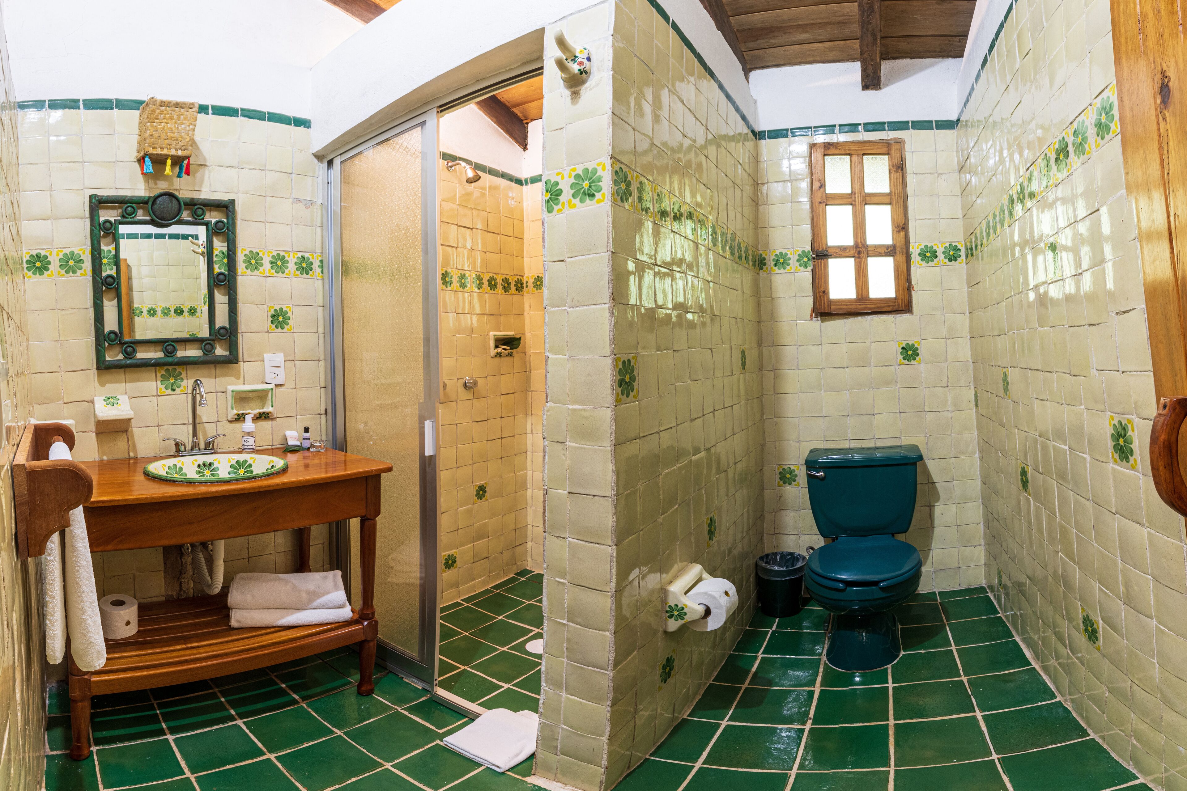 Un baño con tocador de madera, un espejo, inodoro y suelo de azulejos verdes.