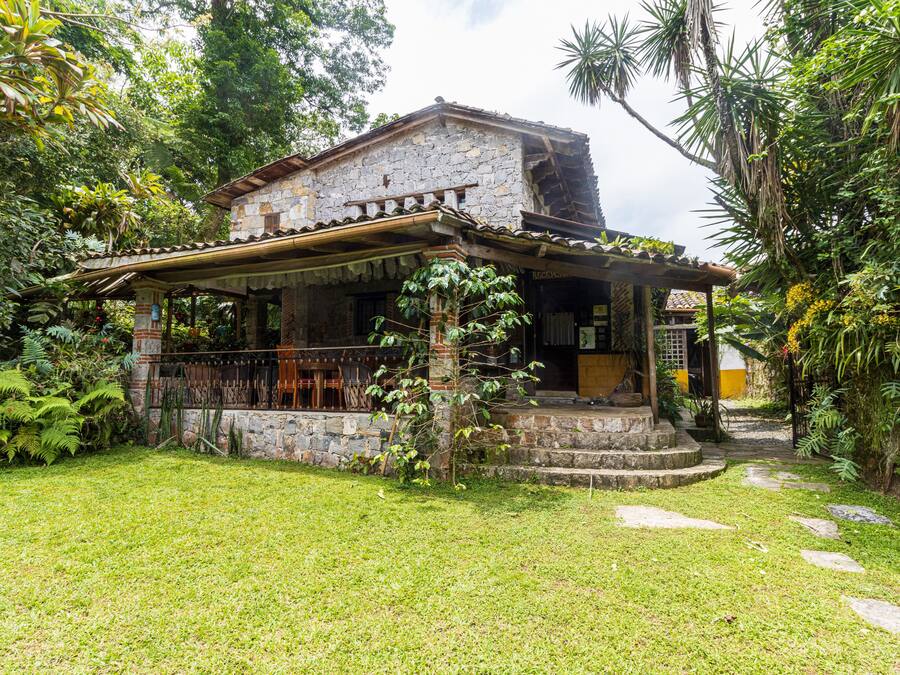 Una casa de piedra rústica con porche cubierto, rodeada de exuberante vegetación y un césped cuidado.