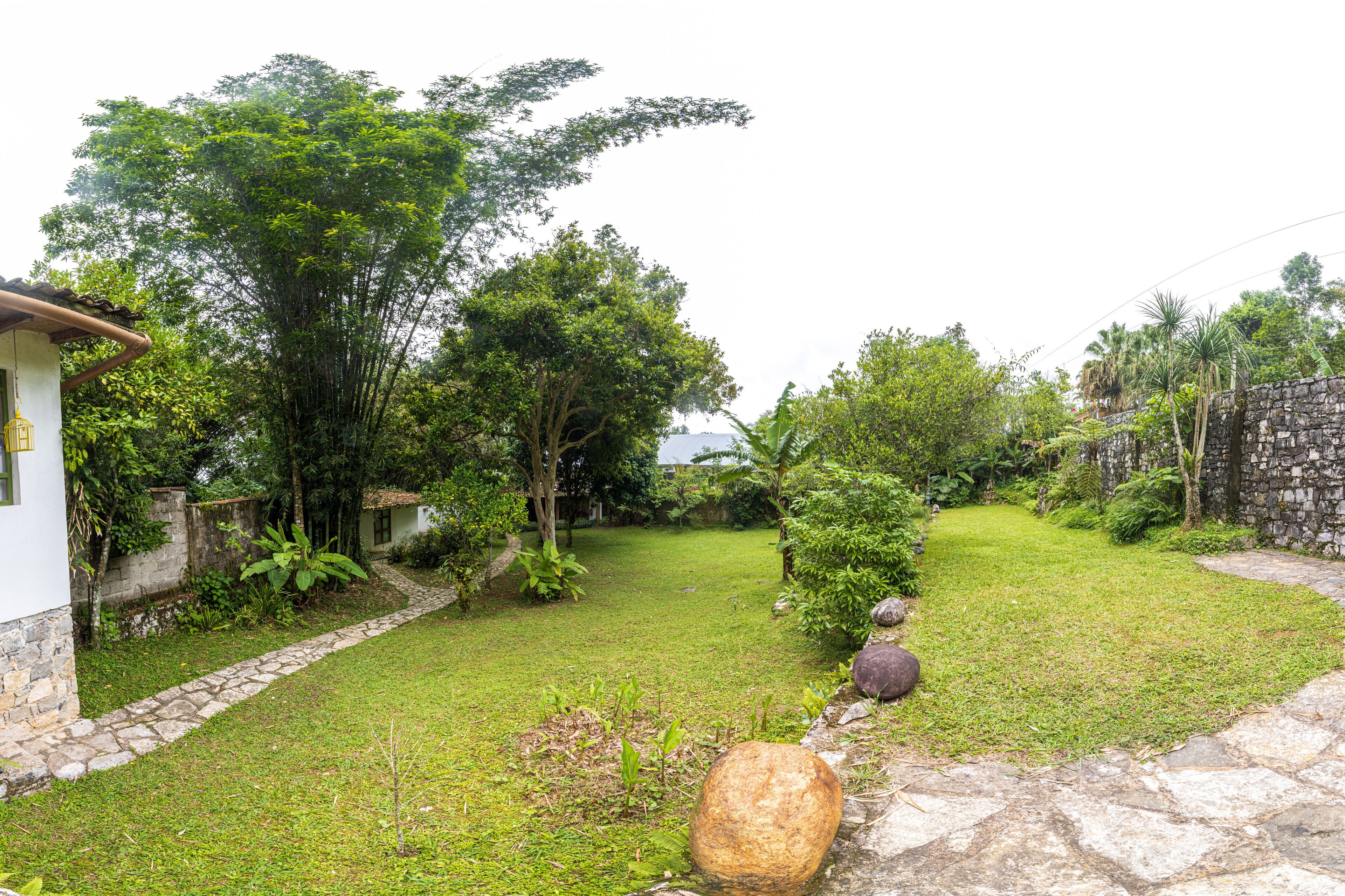 A garden with a stone pathway, lush greenery, and a small white building.