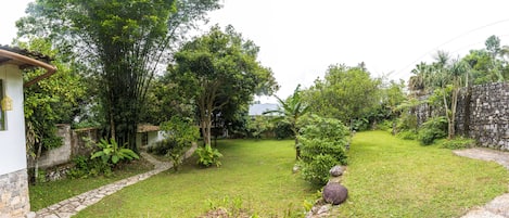 A garden with a stone pathway, lush greenery, and a small white building.
