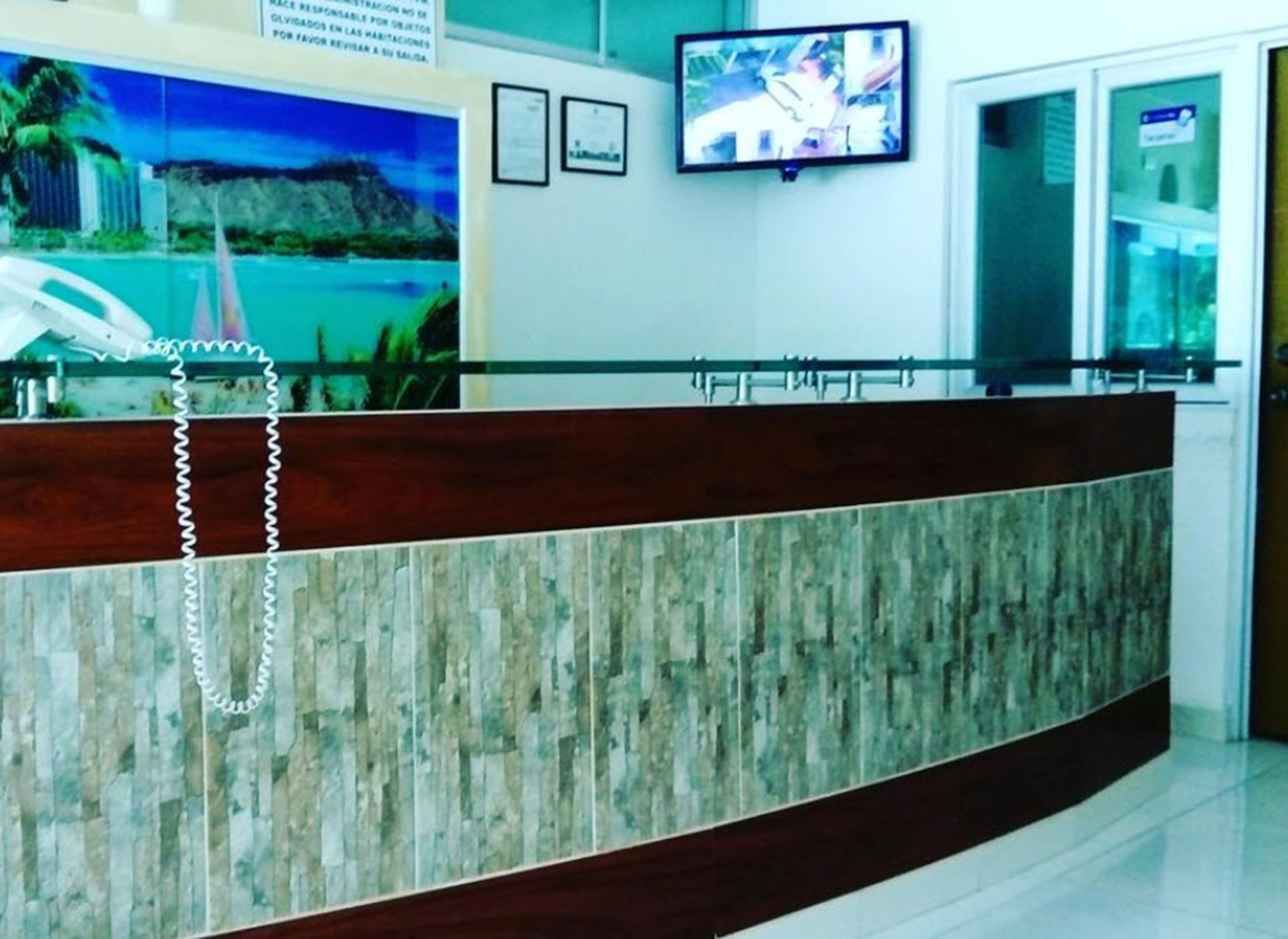 Una reception con finitura in legno e un divisorio in vetro. Un televisore è montato sulla parete sopra il bancone.