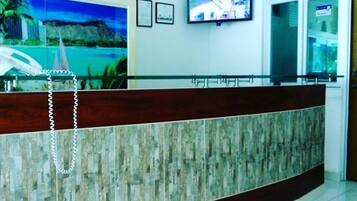 Una reception con finitura in legno e un divisorio in vetro. Un televisore è montato sulla parete sopra il bancone.