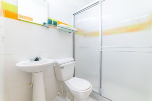 Un baño con lavamanos, inodoro y cabina de ducha blancos.
