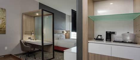 A hotel room with a desk, chair, bed, and a coffee maker on the counter.