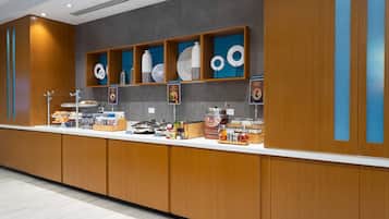 A modern breakfast bar with wooden cabinets, a variety of food items, and decorative plates on shelves.