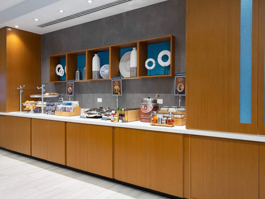 A modern breakfast bar with wooden cabinets, a variety of food items, and decorative plates on shelves.