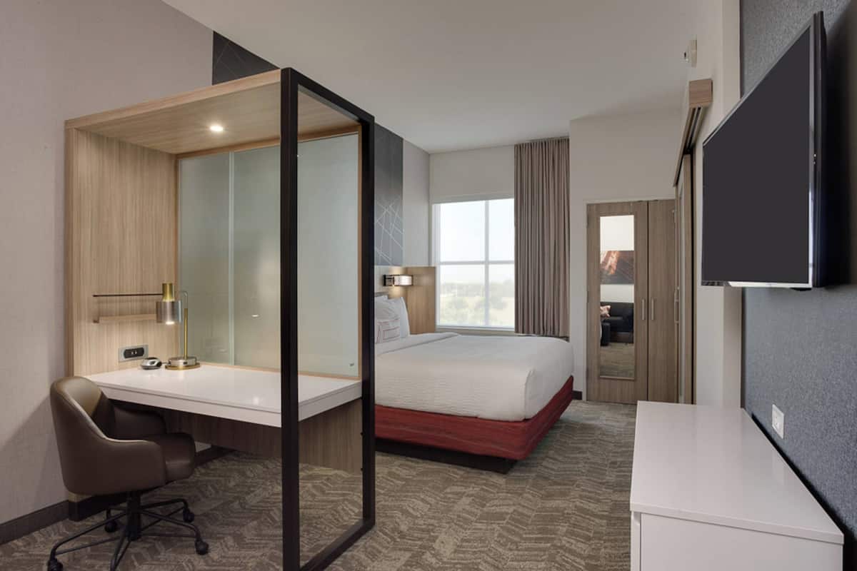 A hotel room with a bed, desk, chair, and a TV mounted on the wall.