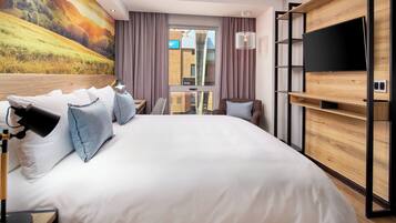 Habitación de hotel moderna con una cama grande, un televisor de pantalla plana montado en una pared de madera, un escritorio con lámpara y vistas a la ciudad por la ventana.