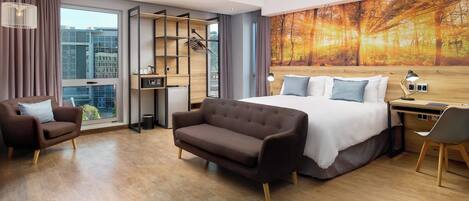 Una habitación de hotel moderna con una cama grande, un sofá, un escritorio y vistas de la ciudad a través de un ventanal.
