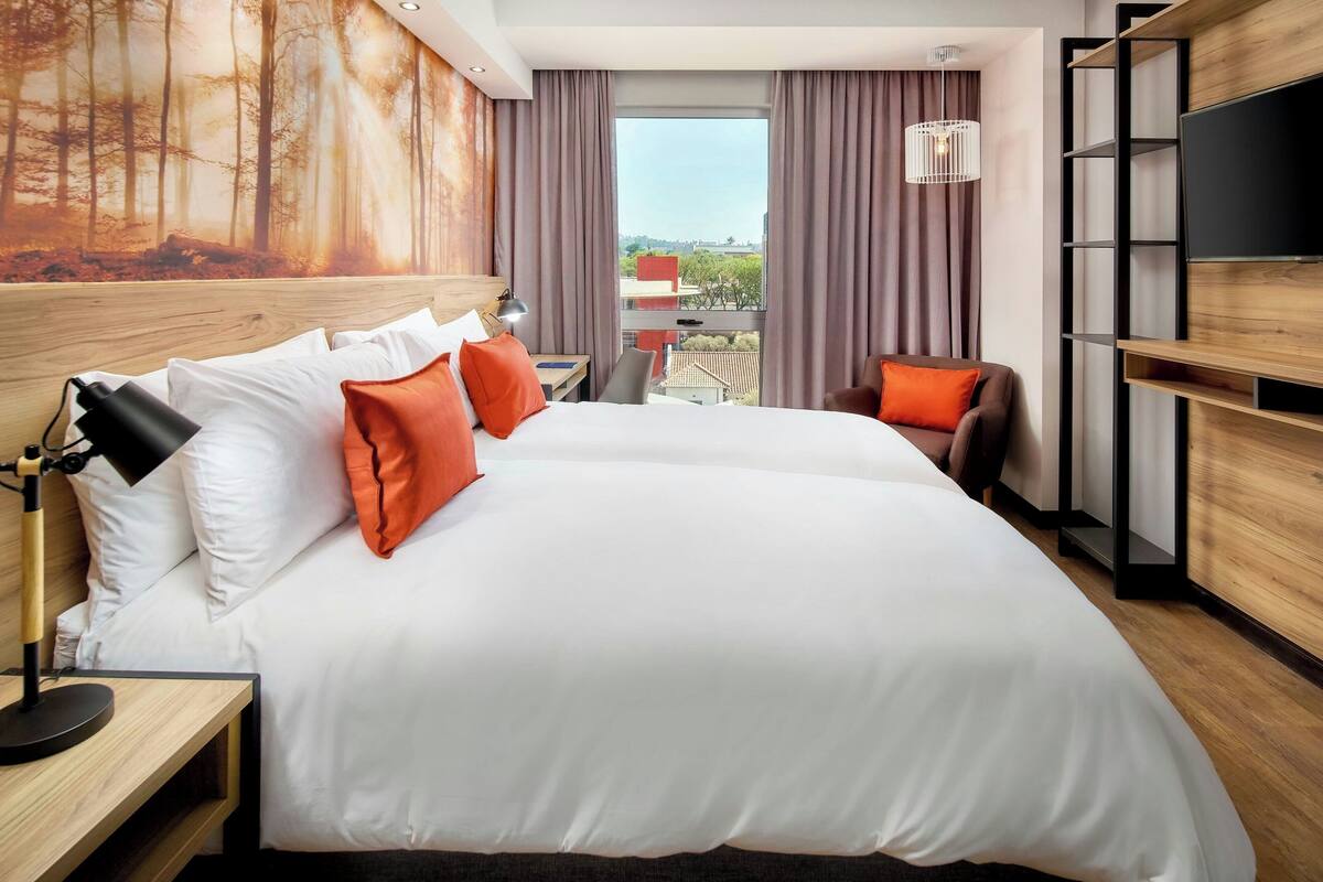Ein Hotelzimmer mit einem großen Bett, einem Schreibtisch, einem Stuhl, einem Fernseher und Blick ins Freie.