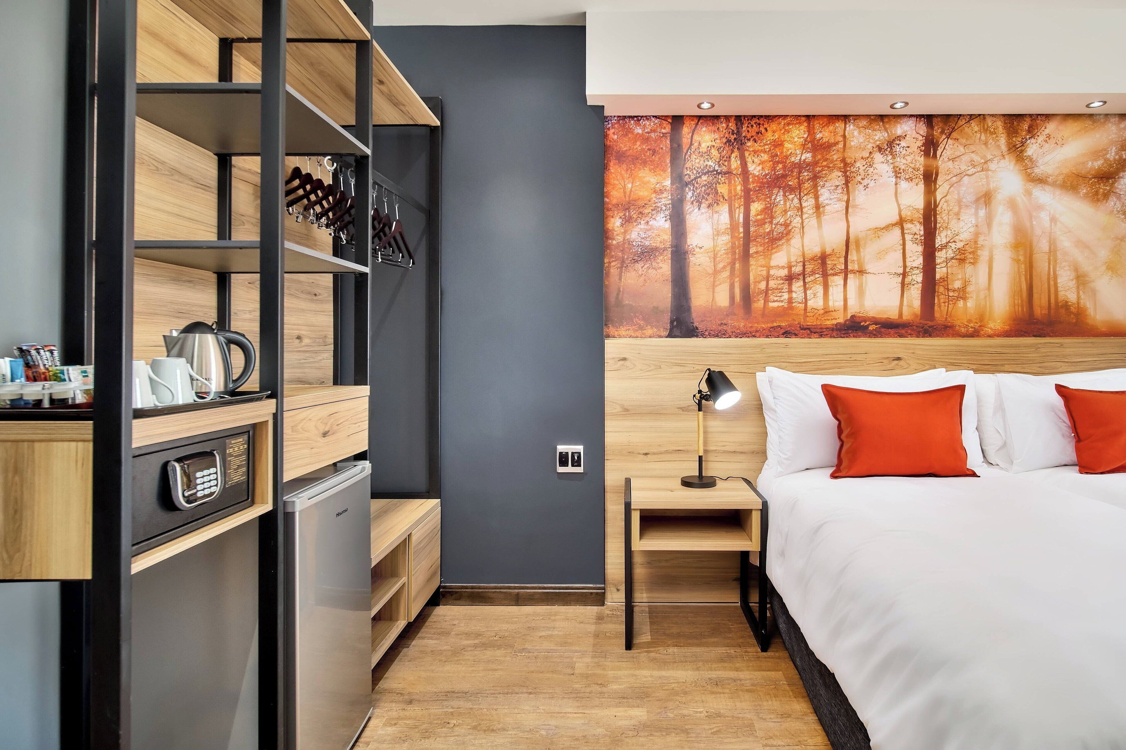 Camera d'albergo moderna con un letto, un comodino, una scrivania, un mini-frigorifero e una mensola a parete.