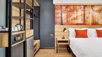 Habitació d'hotel moderna amb un llit, una tauleta de nit, un escriptori, un mini-frigorífic i una prestatgeria penjada a la paret.
