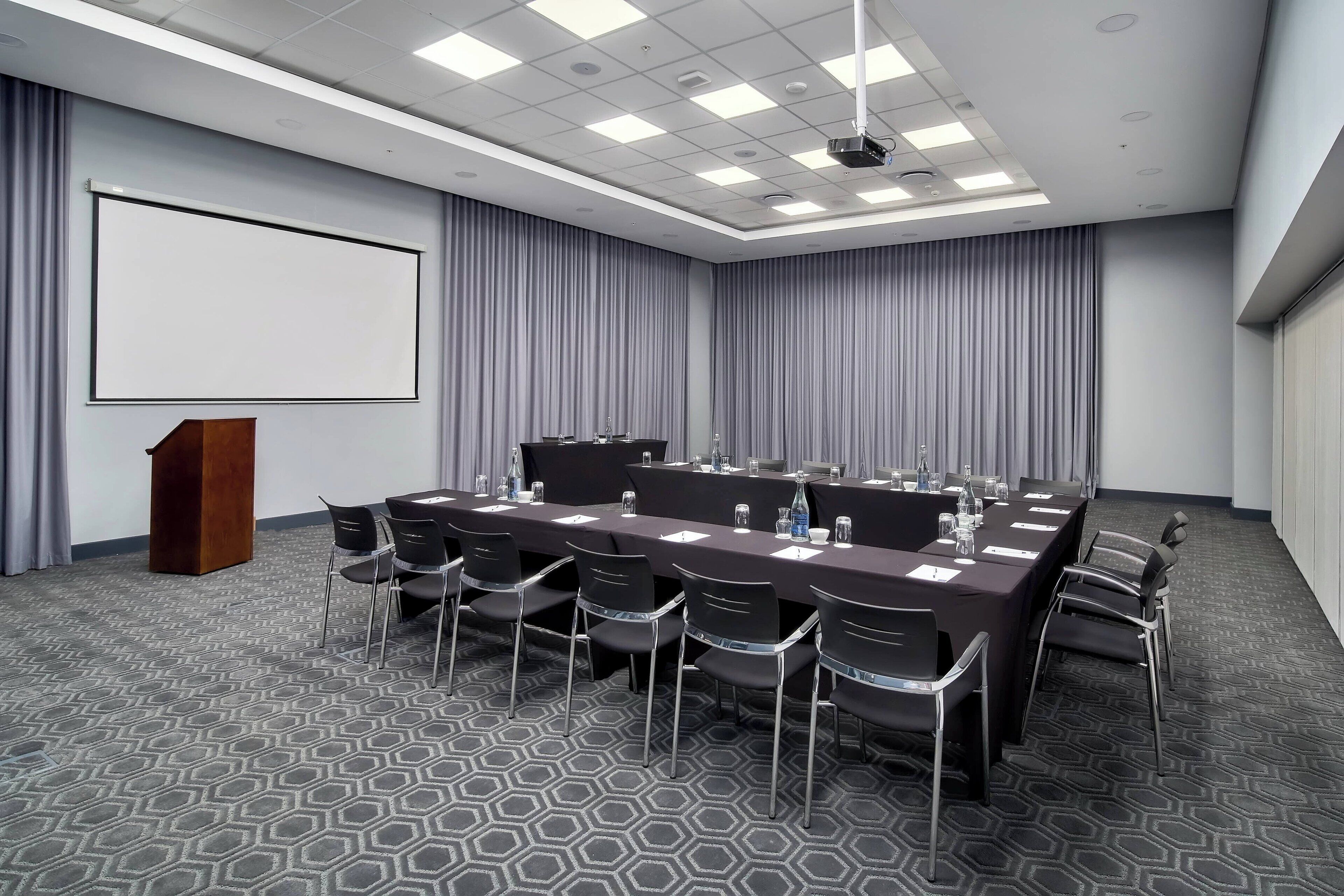 A conference room with a long table, chairs, a podium, and a large screen.