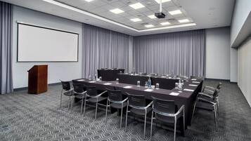 A conference room with a long table, chairs, a podium, and a large screen.