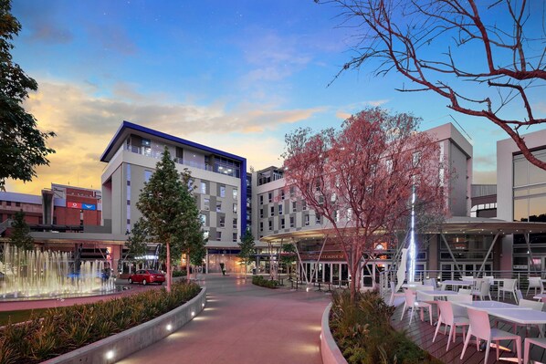 Un hotel moderno con patio central, zona de estar al aire libre y restaurante visible.