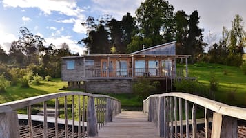 Eine Holzterrasse führt zu einer rustikalen Holzhütte mit Balkon, umgeben von üppigem Grün.