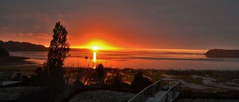 A sunset over a calm body of water with a wooden deck and a railing.