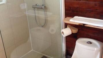 Un baño con ducha de vidrio, inodoro y estante de madera con una toalla.