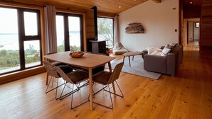 A spacious room with a wooden ceiling, large windows, a dining table with chairs, a sofa, and a fireplace. - Refugio Pullao (Castro)