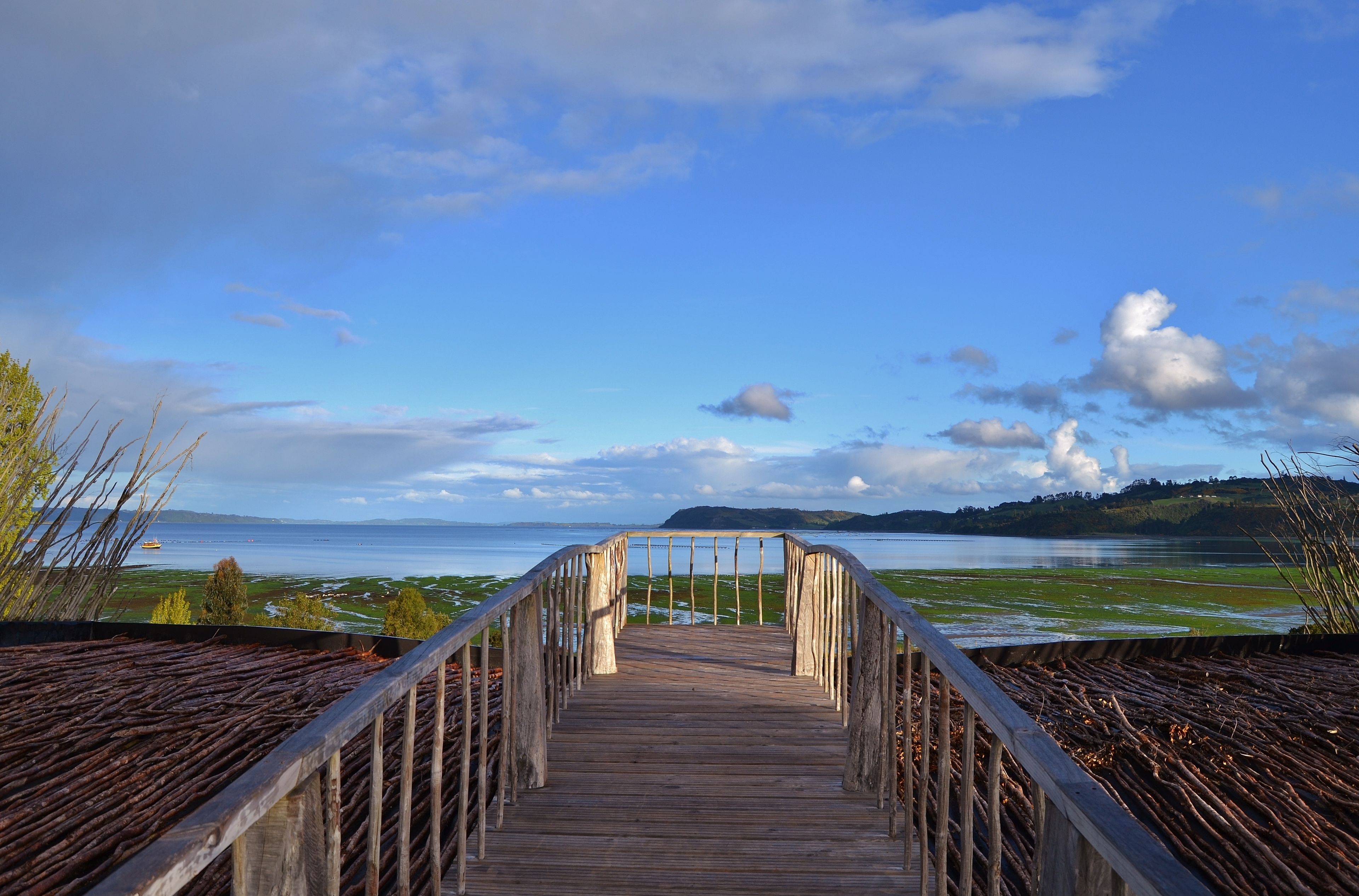A wooden bridge leading to a body of water with a distant island and cloudy sky.