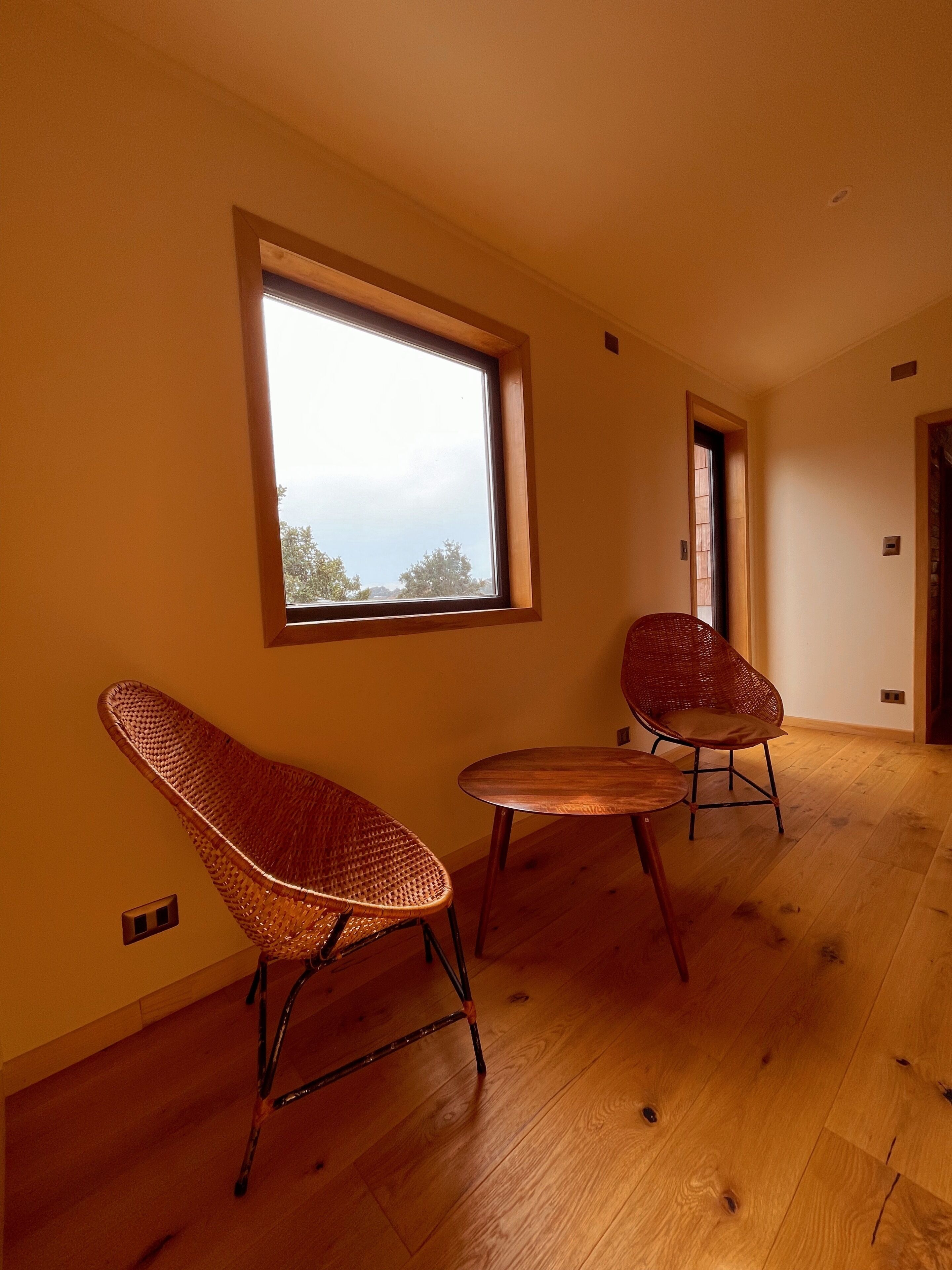 A room with a large window, two wicker chairs, and a small wooden table.