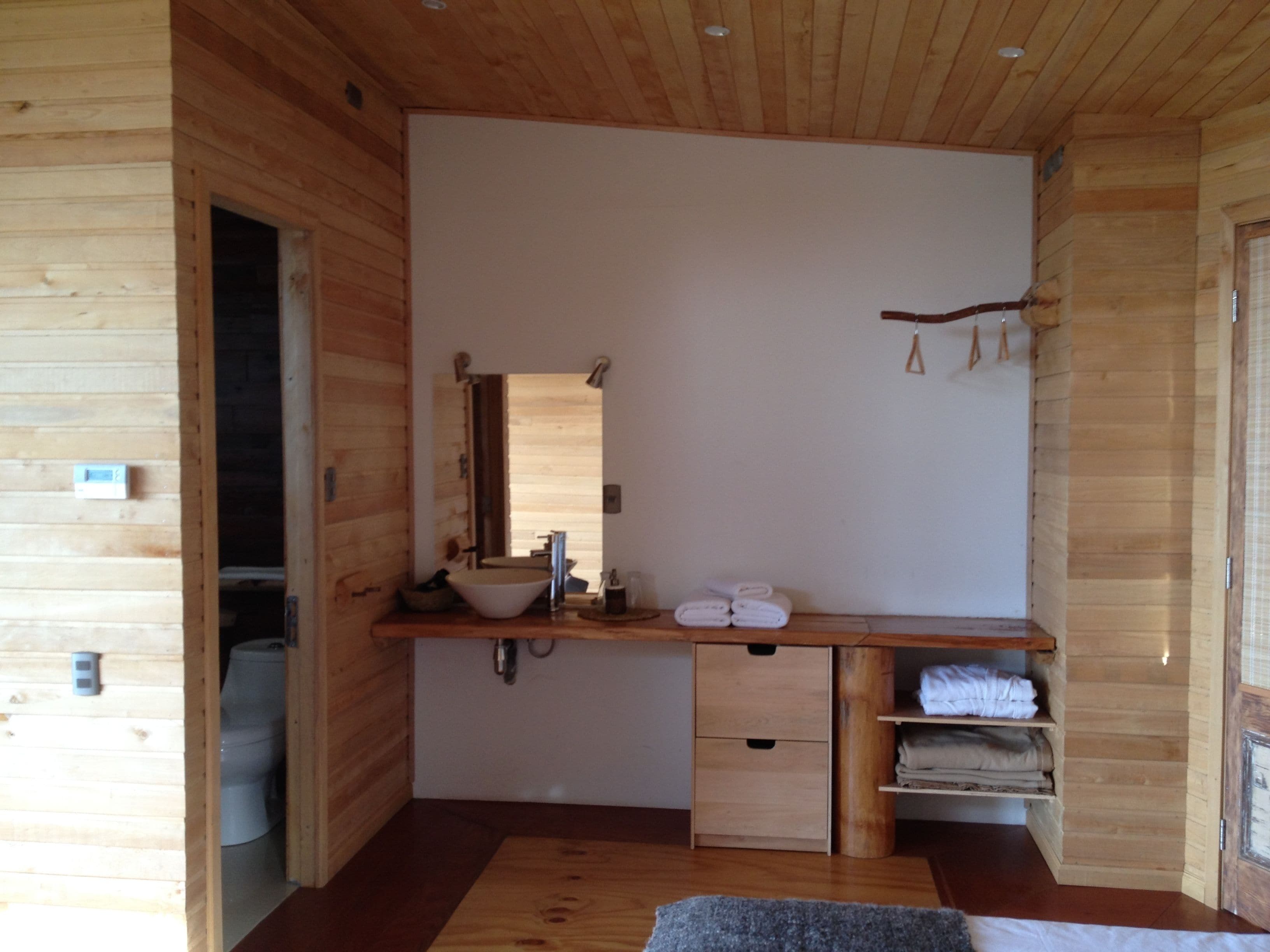A wooden cabin interior with a bathroom, a sink, a mirror, towels, and a shelf.